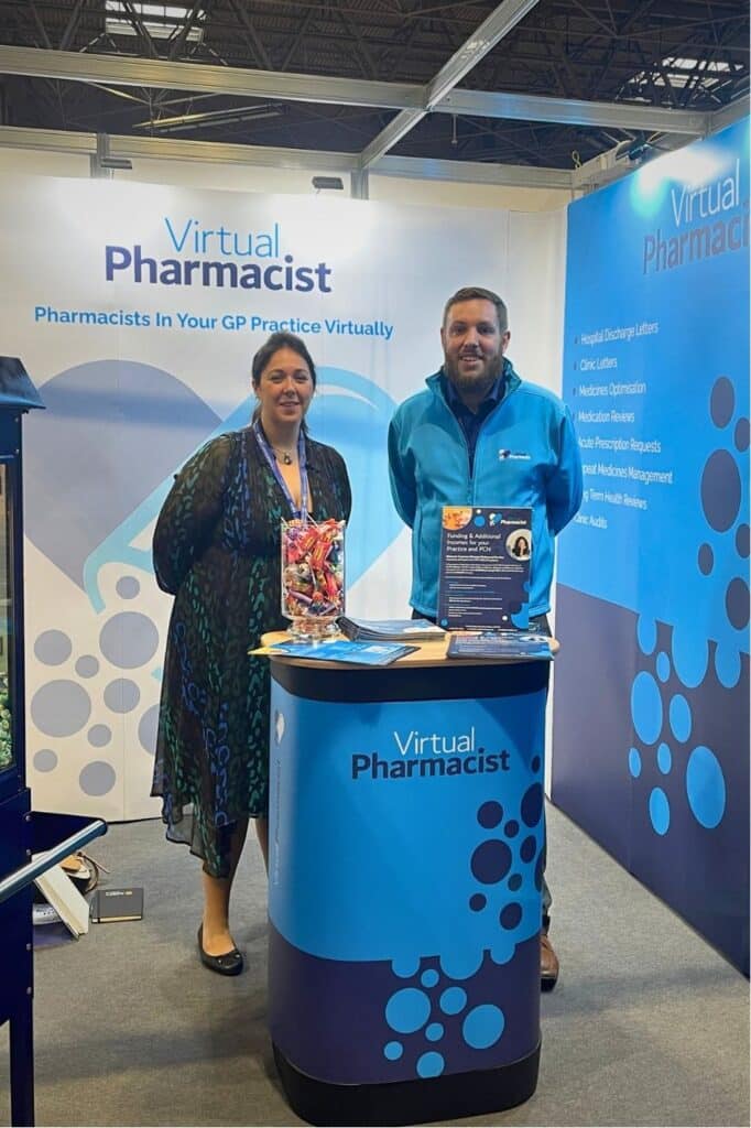 Luke and Laura stand in front of virtual pharmacist table at event