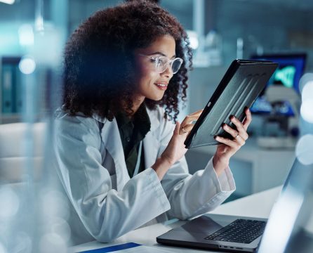 Tablet, laptop and woman scientist in lab working on medical research, project or experiment. Science, career and female researcher with digital technology and computer for pharmaceutical innovation.